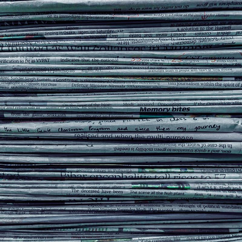 Stack of various newspapers with visible headlines and text.