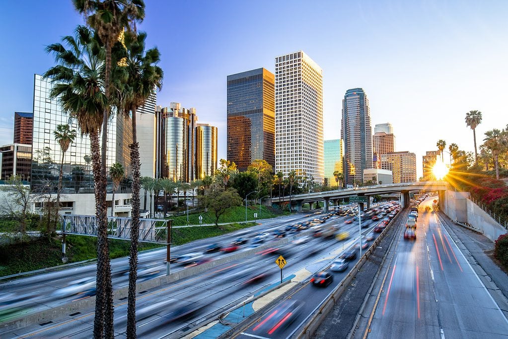 Sunset view over a bustling city highway flanked by skyscrapers and palm trees