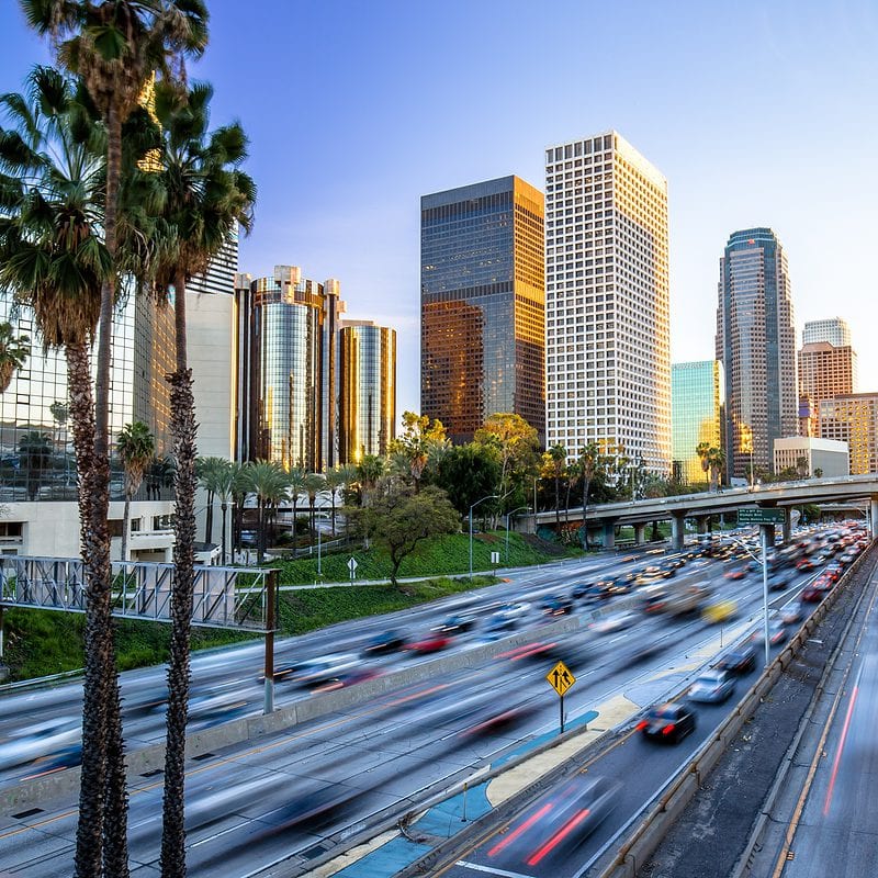 Sunset view over a bustling city highway flanked by skyscrapers and palm trees