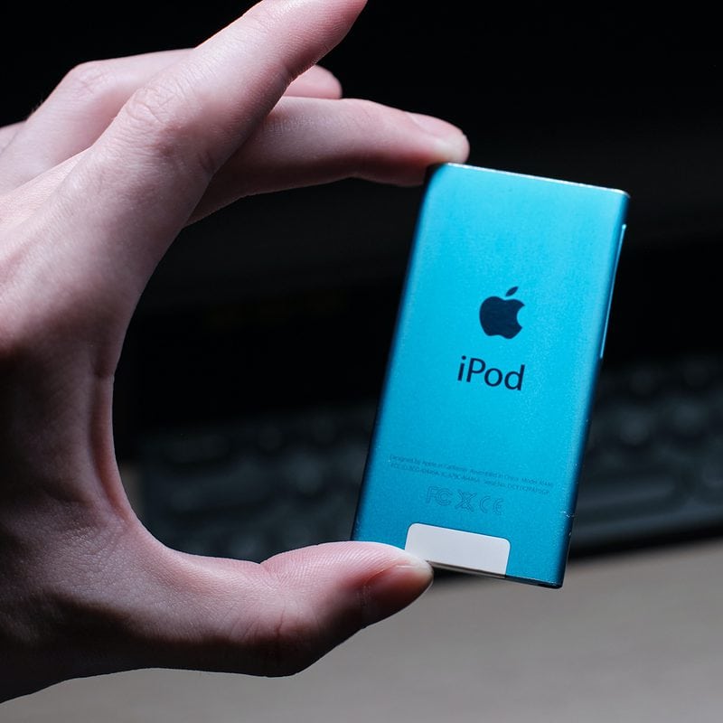 Hand holding a blue iPod with keyboard in background