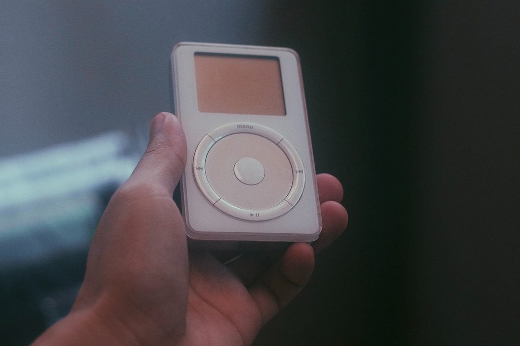 Hand holding a vintage white MP3 player with circular control pad.