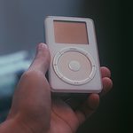 Hand holding a vintage white MP3 player with circular control pad.