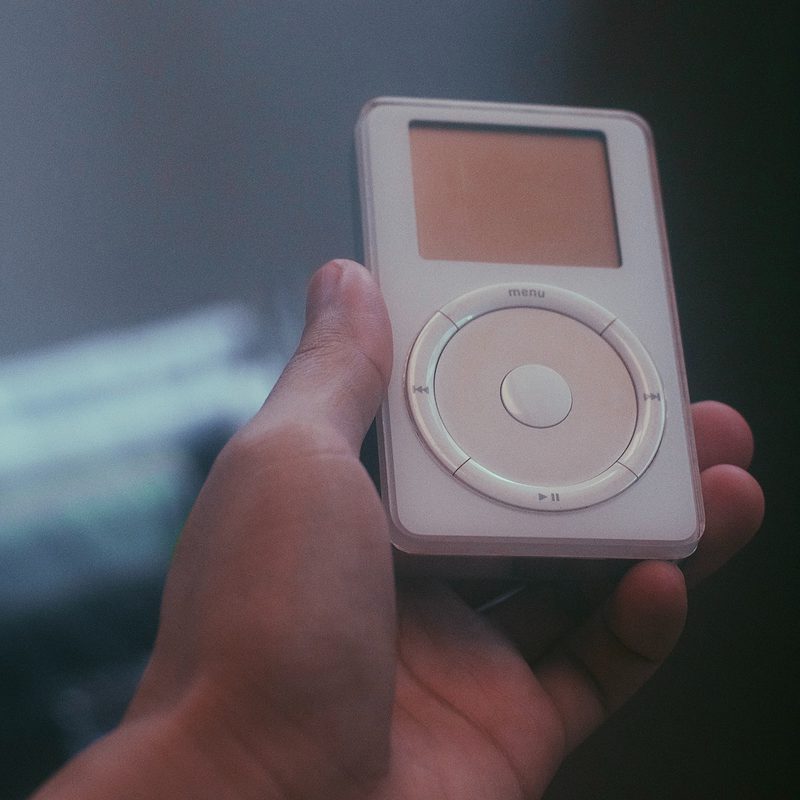 Hand holding a vintage white MP3 player with circular control pad.