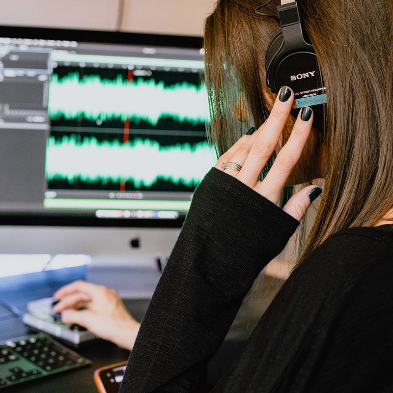 Woman editing audio on computer with waveform on screen and wearing headphones