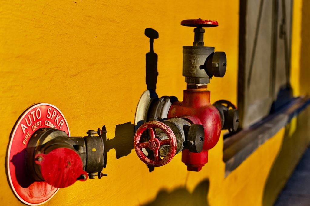 Red and black fire sprinkler valve on a bright yellow wall