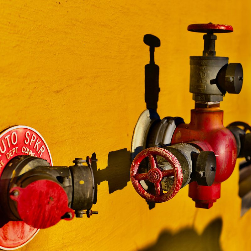 Red and black fire sprinkler valve on a bright yellow wall