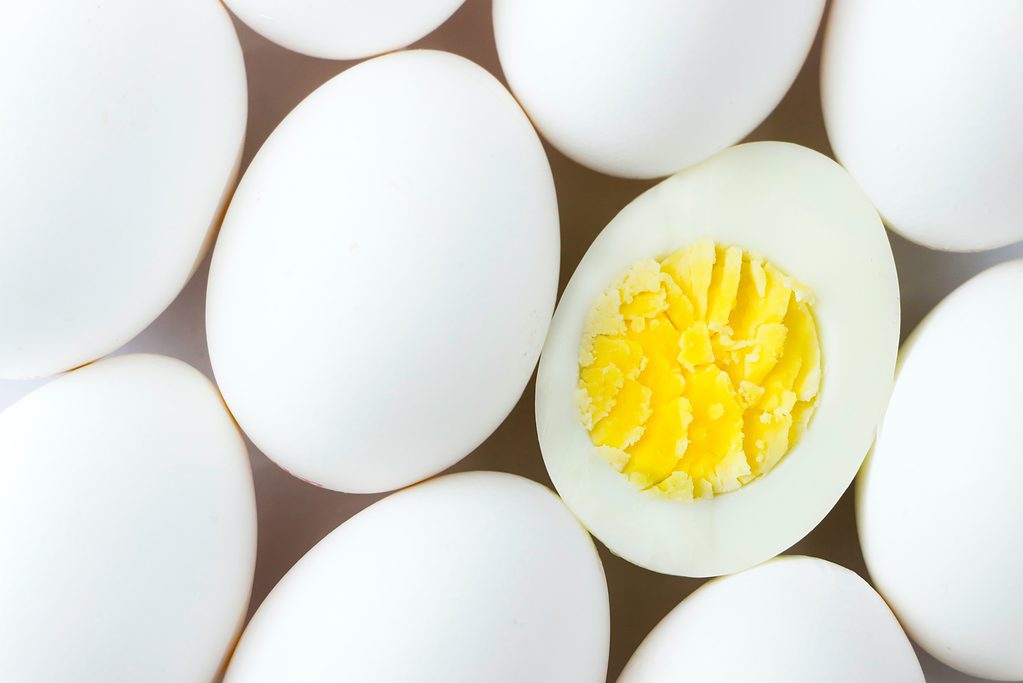 White whole eggs with one cut open showing yolk on beige background