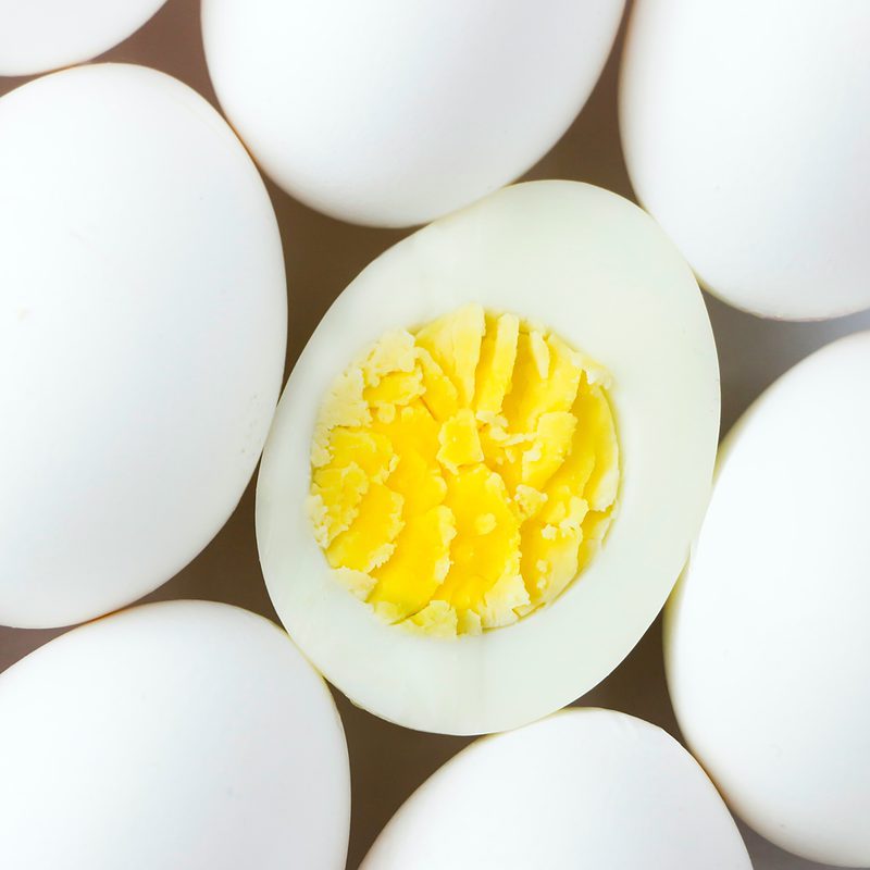 White whole eggs with one cut open showing yolk on beige background