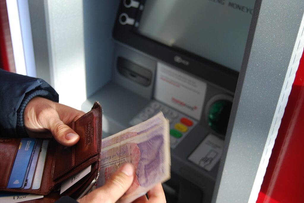 Person withdrawing money from ATM machine with a wallet in hand