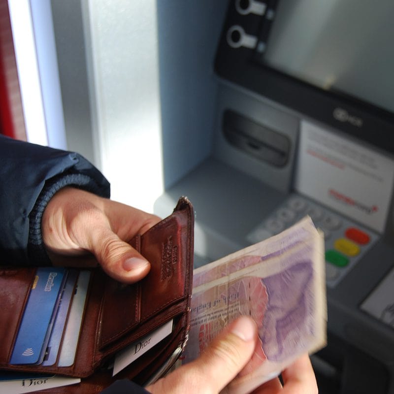 Person withdrawing money from ATM machine with a wallet in hand