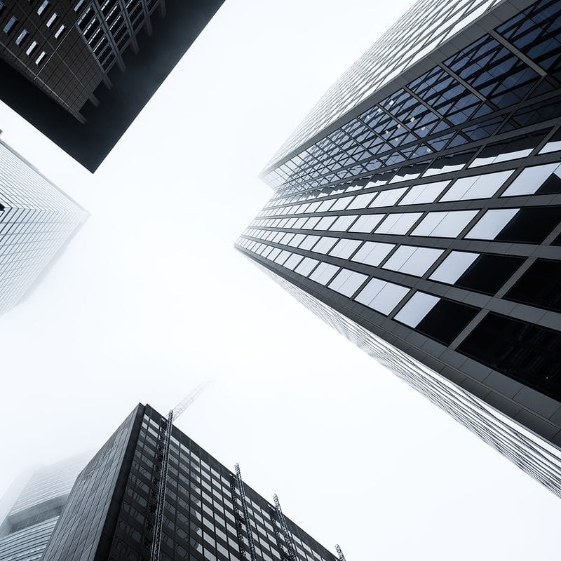 Looking up at towering skyscrapers vanishing into a foggy sky