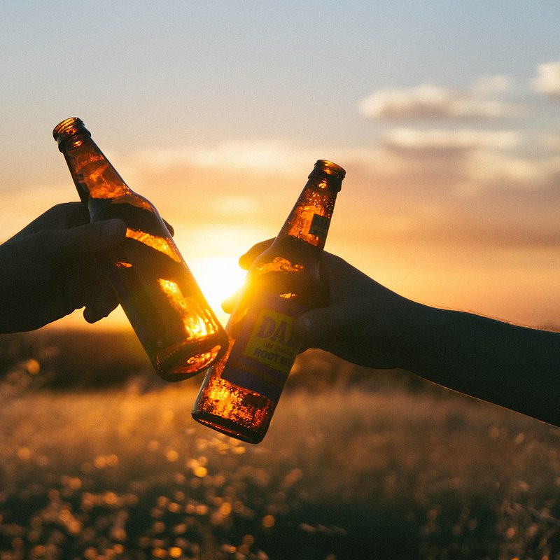 Two people clinking beer bottles at sunset in a field
