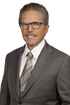 Professional man in suit with tie and glasses smiling against white background.