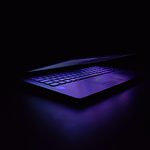Laptop with illuminated keyboard in dark room with purple backlighting