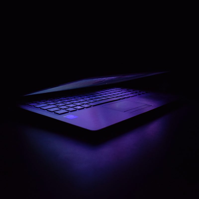 Laptop with illuminated keyboard in dark room with purple backlighting