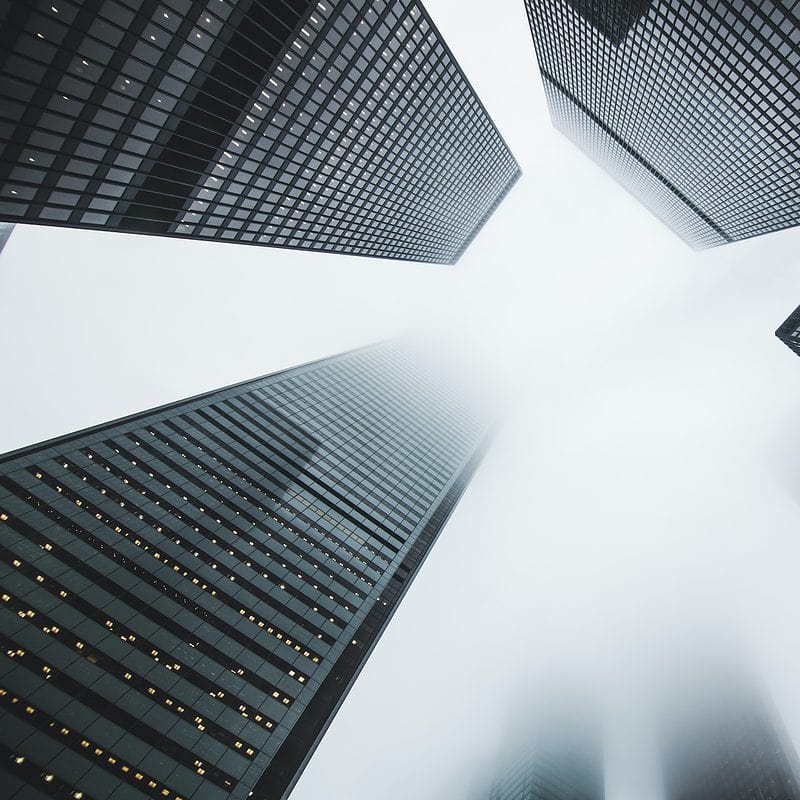 Skyscrapers looming into foggy sky with lights visible in one building