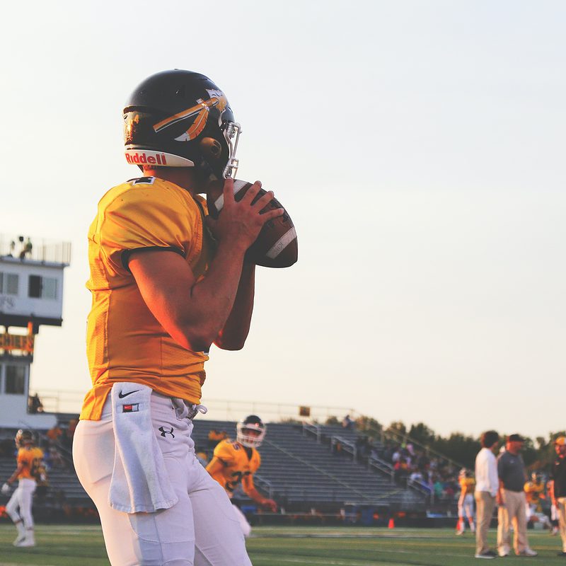 Football player holding ball on field at sunset with team in background