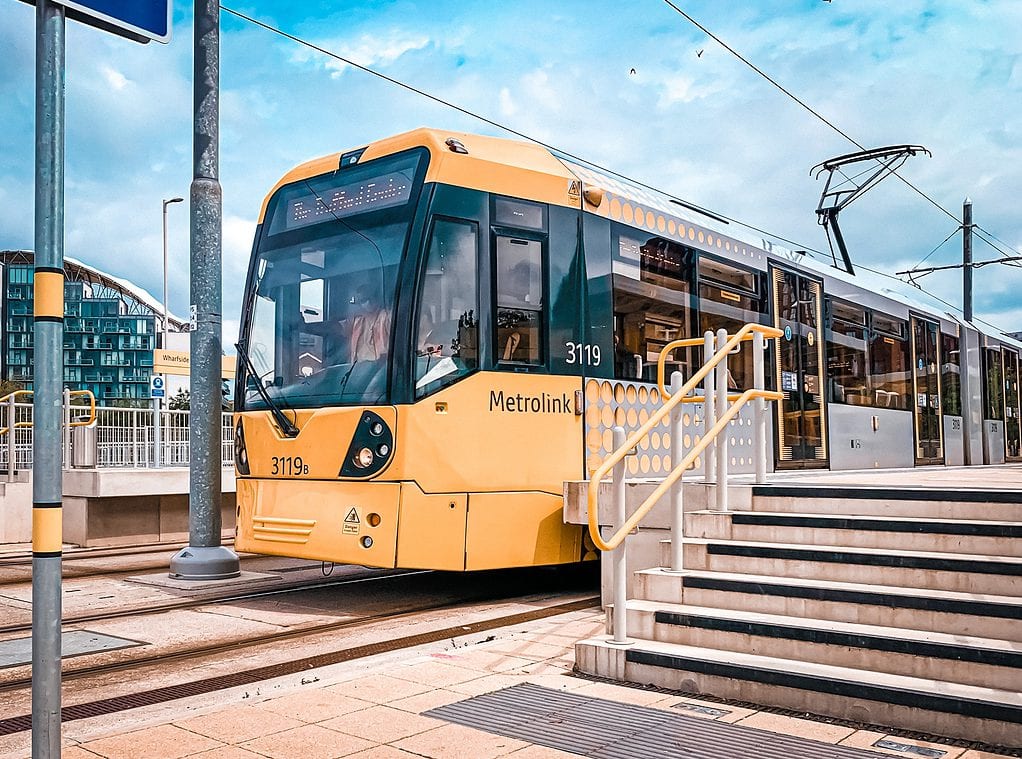 Yellow Metrolink tram at Wharfside stop with modern architecture background