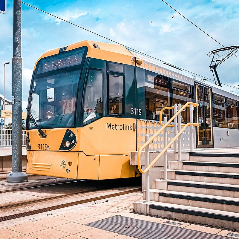 Yellow Metrolink tram at Wharfside stop with modern architecture background