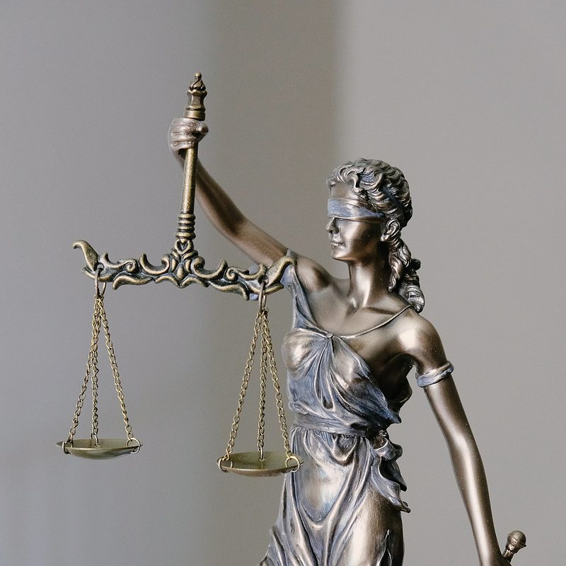 Bronze Lady Justice statue with scales on grey background