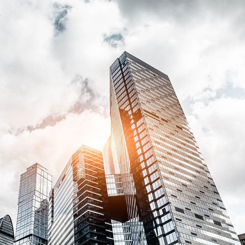 Modern skyscrapers under a cloudy sky with sunlight peeking through