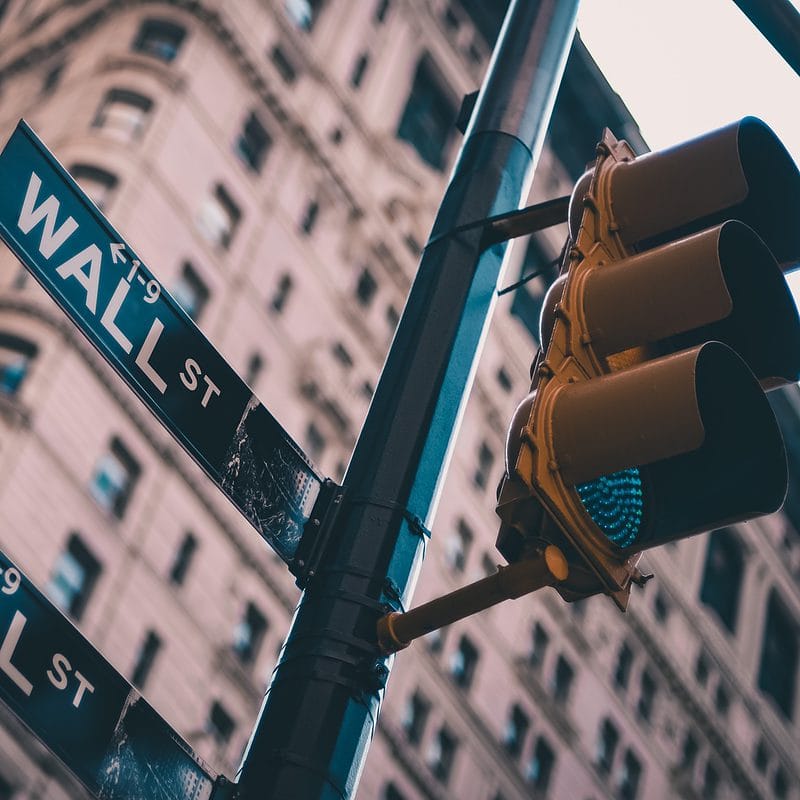 Wall Street sign with traffic light against blurred buildings.