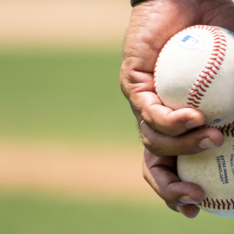 Close-up of a hand holding a baseball with partial view of striped uniform.