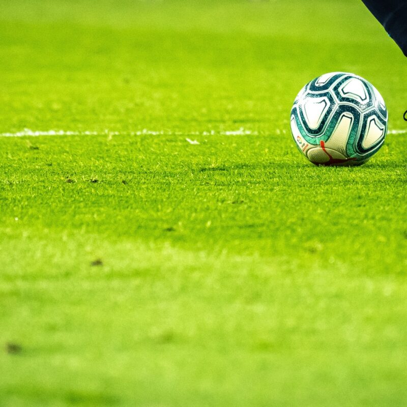 Soccer player dribbling ball on green pitch in close-up view