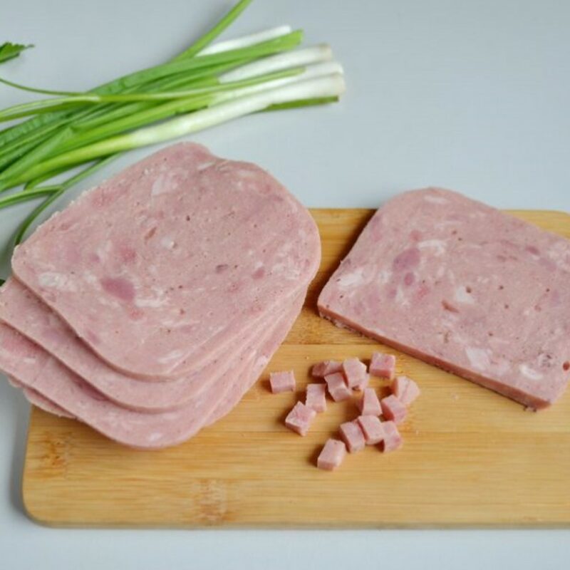 Sliced ham and diced cubes on cutting board with fresh parsley