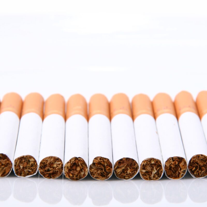 Row of unlit cigarettes with orange filters on white background
